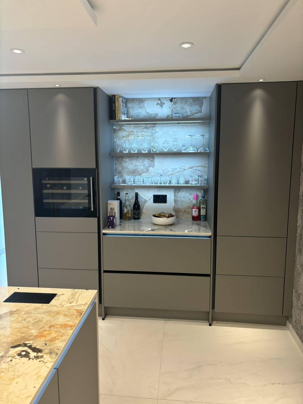 Fitted drinks nook with glass shelving and marble worktop