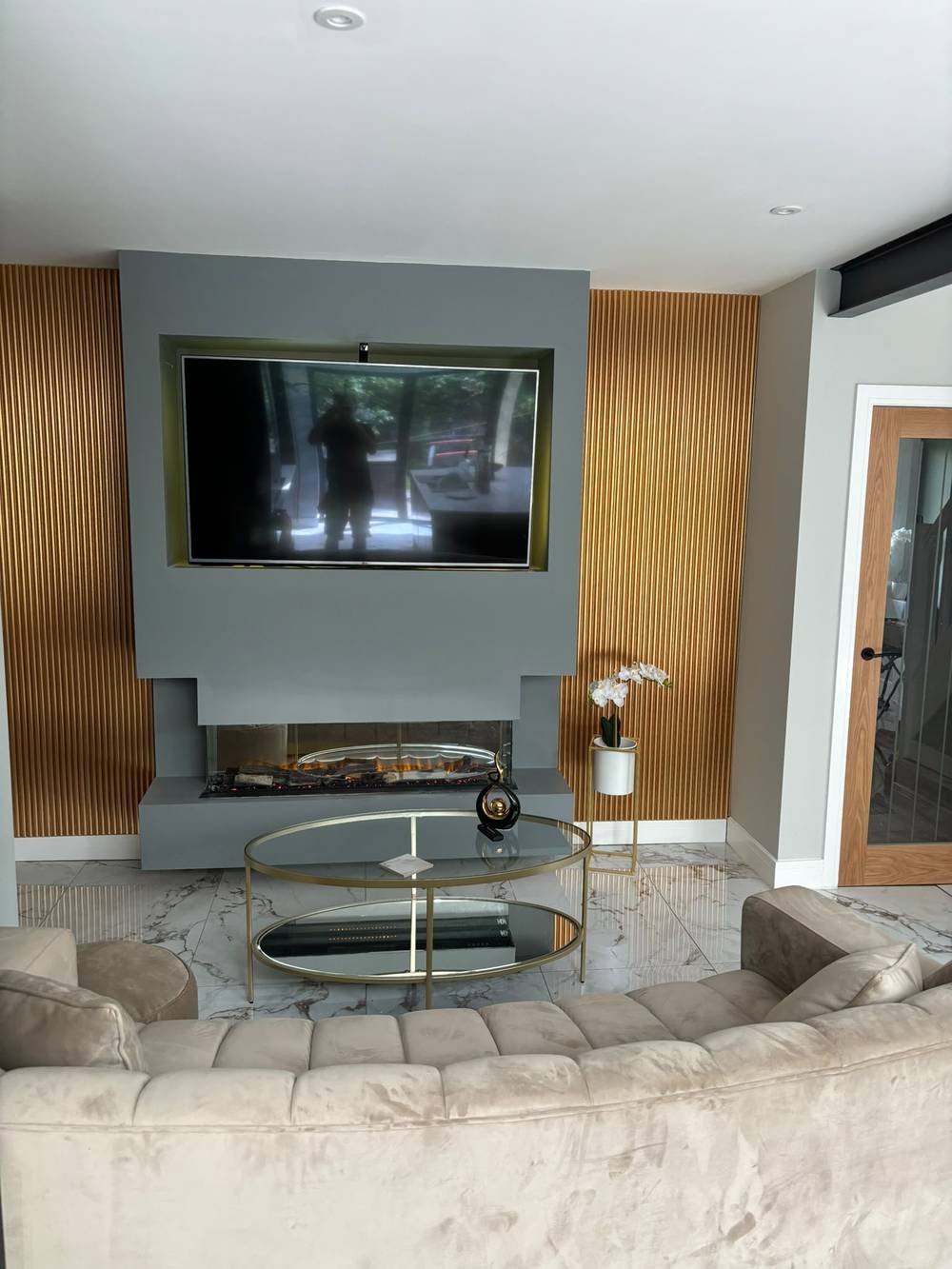 Media wall with slatted panelling, gold accents and a bay fireplace